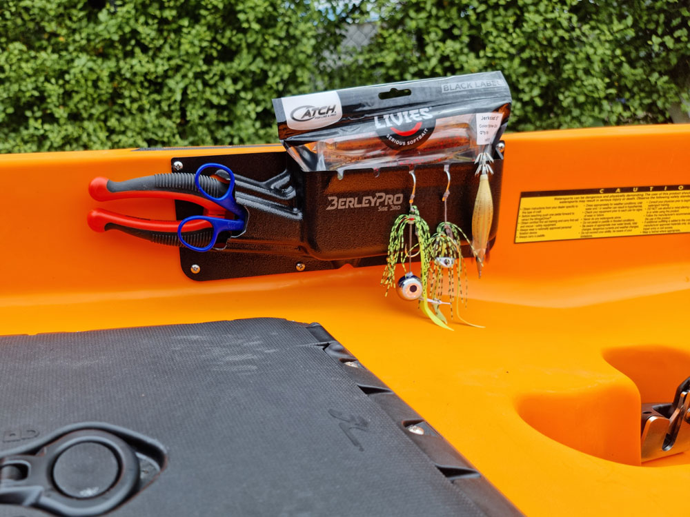 Feast your eyes on this stunning orange kayak, perfectly decked out with the ultimate Side Bro - Tool and Tackle Organizer! Loaded up with all the essentials like scissors, pliers, a selection of fishing lures, and even a handy lure package, you're all set to make your next adventure unforgettable. And let's not forget the lush green foliage in the background – it’s nature’s way of amplifying your daring spirits!.