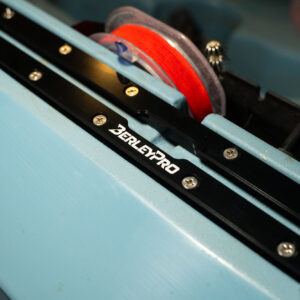Get ready to dive into the details with a close-up of the BerleyPro Upgraded Billet Aluminum Track Mount. Set against a sleek blue backdrop, this beauty shines while a red fishing line spool waits eagerly in the background. Perfectly crafted for your ultimate adventure, it's all about precision and performance right here!.