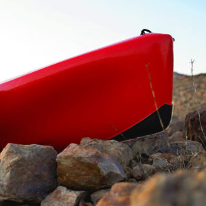 Get up close and personal with your kayak as it rocks the sleek Bumper Bro Kayak Keel Guard, confidently perched on rugged rocky terrain beneath a crystal-clear sky.