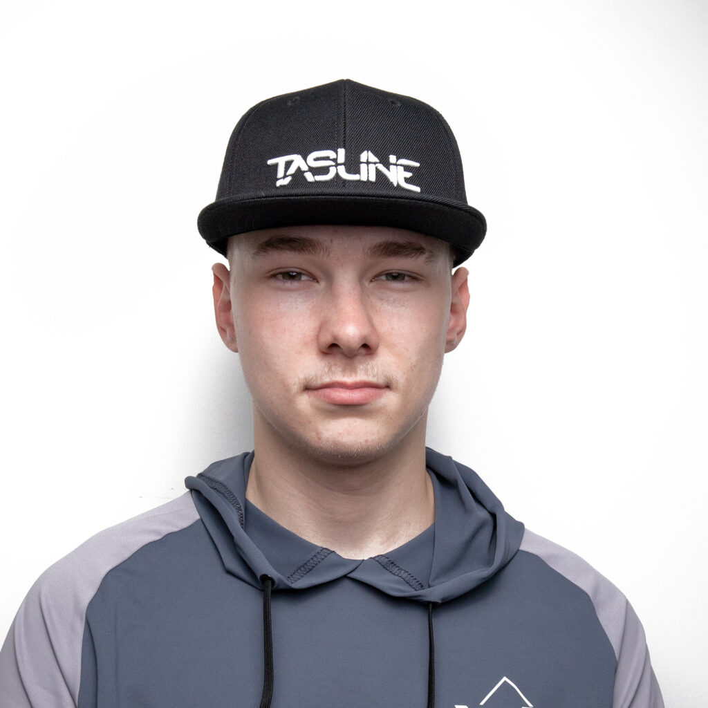 A sleek operator in a black Tasline Cap Flat Bill, showcasing that iconic "TASKLINE" logo with pride, pairs it effortlessly with a chill blue-gray hoodie. All set against a clean white backdrop, this look is pure style perfection straight out of the BerleyPro playbook!.